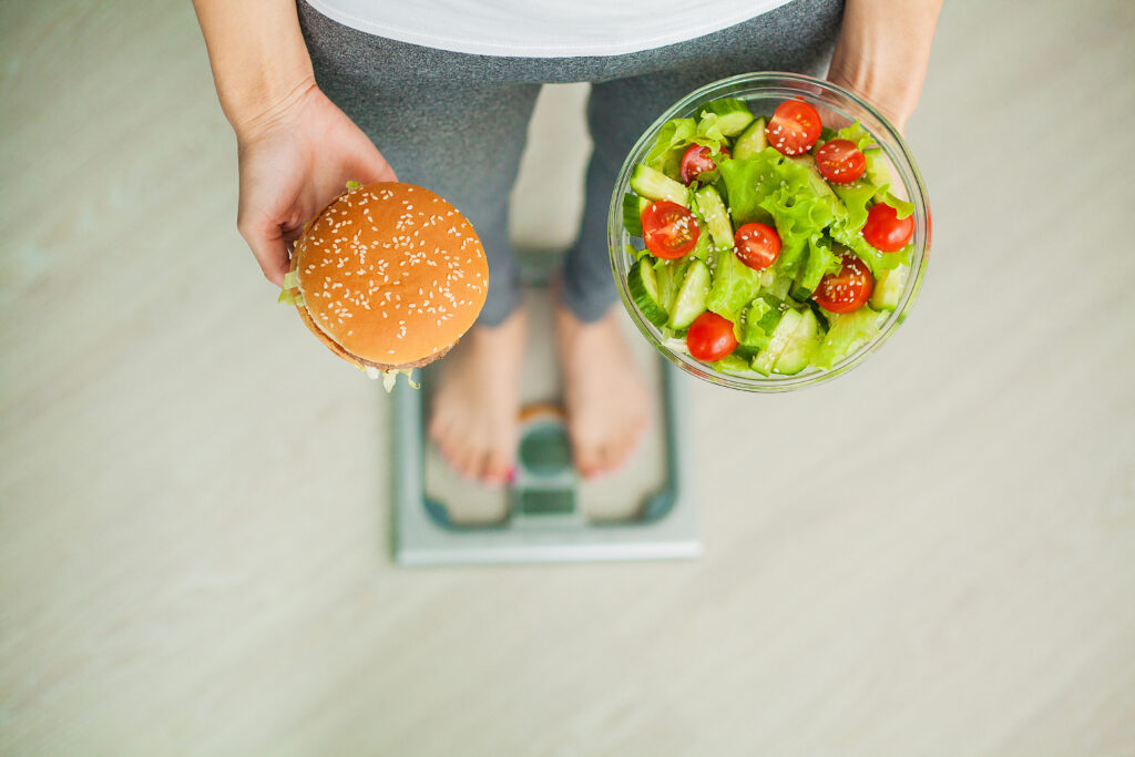 Une femme se tenant sur une balance compare un hamburger et une salade